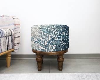 May include: A small, round wooden stool with a botanical print. The top of the stool features a watercolour-style pattern of blue and green leaves. The stool has a dark brown, turned-leg base.