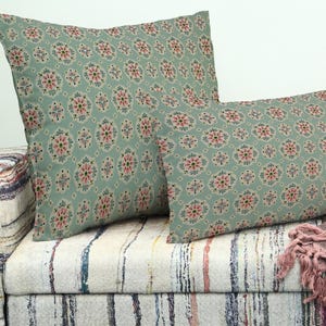 Könnte beinhalten: Zwei dekorative Kissen mit einem Blumenmuster in Grün-, Rosa- und Cremetönen. Die Kissen liegen auf einem gemusterten Sofa. Die Kissen haben ein weiches, einladendes Aussehen, perfekt, um jedem Wohnraum einen Hauch von Eleganz zu verleihen.