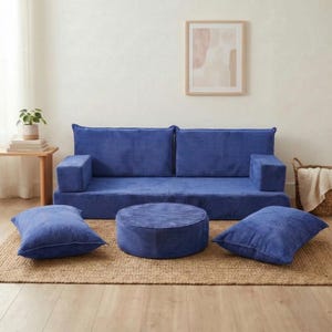 May include: A modular blue corduroy sofa set with a two-seat base, two armrests, a round ottoman, and two square pillows. The furniture is arranged on a woven jute rug, creating a cozy living space. A framed abstract art piece hangs on the wall.