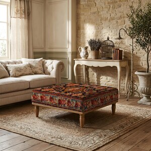 May include: A square ottoman featuring a dark, multi-coloured floral pattern on a fabric upholstery. The piece is supported by four light-toned wooden legs with a turned design, providing a stable base for the low-profile, cushioned seat.