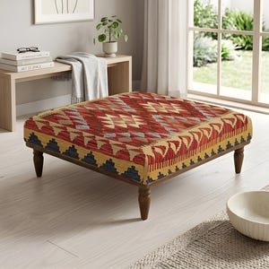 Peut inclure: Un pouf carré doté d'un dessus en textile tissé avec un motif géométrique dans des tons de rouge, jaune, bleu et crème. La pièce est soutenue par quatre pieds en bois brun foncé au design tourné, offrant une base stable pour le siège.