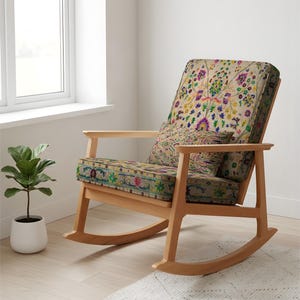 May include: A wooden rocking chair with a floral patterned cushion and backrest. The chair has a light wood frame and armrests. A small pillow with a matching floral pattern sits on the seat. A small potted plant is next to the chair.