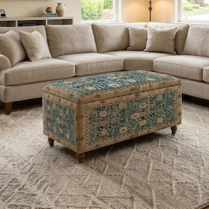 May include: A beige sectional sofa with multiple cushions and a patterned ottoman. The ottoman has a teal and beige floral design. The rug has a geometric pattern. The room is well-lit with natural light.