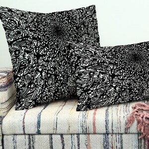 May include: Two cushions with a black and white abstract pattern are placed on a patterned sofa. The cushions have a detailed, swirling design, contrasting with the sofa's neutral colours. Ideal for home decor.
