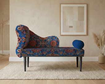 May include: A blue chaise lounge with a patterned fabric in red, orange, and white. The chaise has a curved back and a small blue bolster pillow. It sits on four dark gray legs and a light-colored rug.