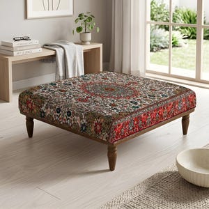 Peut inclure: Un pouf carré arborant un motif floral et géométrique détaillé et multicolore dans des tons de rouge, bleu et crème. Le meuble est soutenu par quatre pieds en bois tourné brun foncé, offrant une base basse à ce siège rembourré.