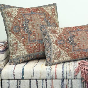 May include: Two decorative throw pillows with a vintage rug design in shades of red, blue, and beige rest on a patterned sofa. The pillows have a rectangular and square shape, with a detailed border.