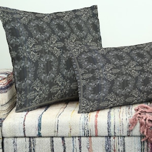 Pode incluir: Duas almofadas decorativas com um padrão floral cinza escuro repousam sobre um sofá listrado. As almofadas têm formato quadrado e retangular. Uma manta com franjas está sobre o sofá.