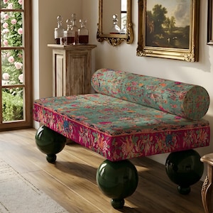 May include: A rectangular bench featuring a teal and magenta floral patterned fabric upholstery with a matching cylindrical bolster pillow. The bench is supported by four large, glossy, dark green spherical legs.