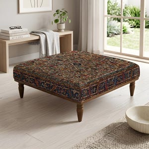 Peut inclure: Un pouf carré recouvert d'un tissu à motifs complexes et sombres, décliné dans des tons profonds de rouge, de bleu et de brun. Le meuble repose sur quatre pieds en bois tourné d'une finition brun moyen, assurant une base stable à l'assise.