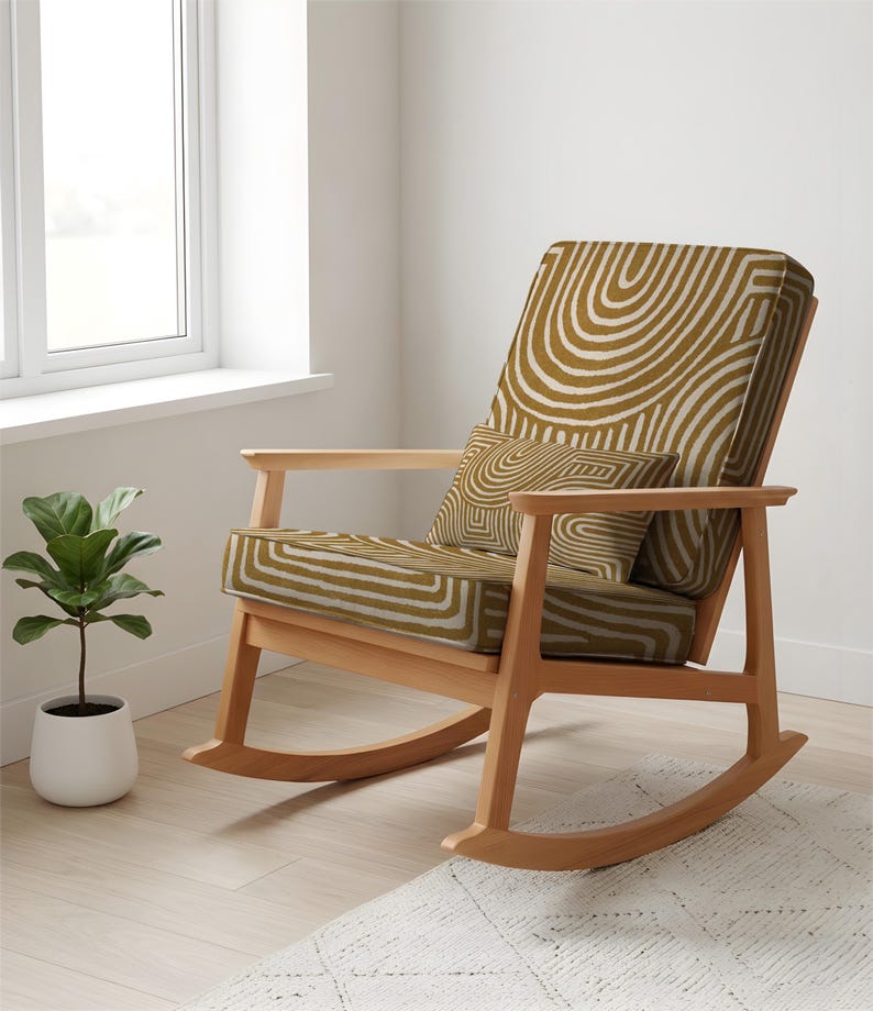 May include: A wooden rocking chair with a mustard cushion and pillow, patterned with white curved lines. The chair has a light wood frame and armrests. A small potted plant sits near a window.