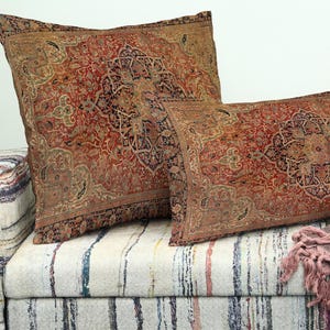 Puede incluir: Dos cojines decorativos rectangulares con un diseño de alfombra vintage en tonos rojos, marrones y beige. Los cojines presentan patrones intrincados. Se encuentran sobre un sofá tapizado a rayas, creando un aspecto acogedor y elegante.