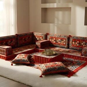 Peut inclure: Un canapé d'angle à motifs rouges et noirs avec des coussins assortis et une table basse. Le canapé est placé sur un tapis blanc, créant un coin salon confortable. Les coussins et la table ont un motif géométrique.
