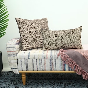 May include: A bench with a striped pattern and wooden legs, with two leopard print cushions and a fringed throw. A potted palm tree is on the left.