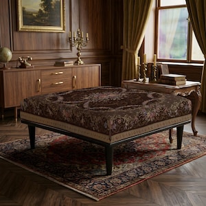 May include: A square ottoman featuring a dark brown fabric top with a detailed floral pattern in shades of pink, blue, and cream. The piece is supported by four tapered black wooden legs and includes a light beige border along the lower edge.