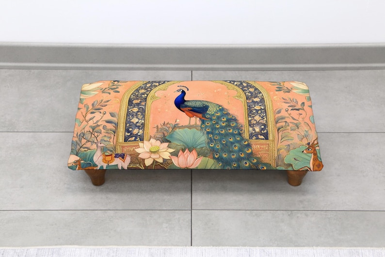 May include: Rectangular footstool with a vibrant peacock design. The peach-colored fabric features a peacock, lotus flowers, and other decorative elements. The wooden legs provide support. A decorative piece for any room.