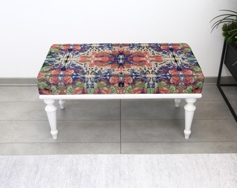 Puede incluir: Un banco rectangular con estructura de madera blanca y cuatro patas curvas. La parte superior acolchada presenta un colorido patrón abstracto en tonos rojos, azules, verdes y beige.