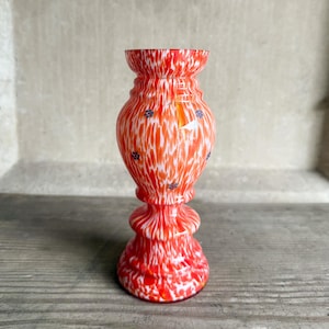 May include: A red and white glass vase with a speckled pattern. The vase has a wide base and a narrow neck.