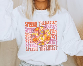 May include: White sweatshirt with a colorful smiley face and the text "Speech Therapist" repeated in a retro font.