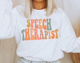 May include: White sweatshirt with the text "SPEECH THERAPIST" in colorful retro-style lettering.