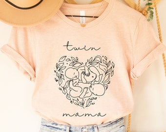 May include: A light pink t-shirt with the text "twin mama" and a black line drawing of two babies inside a heart shape with leaves.
