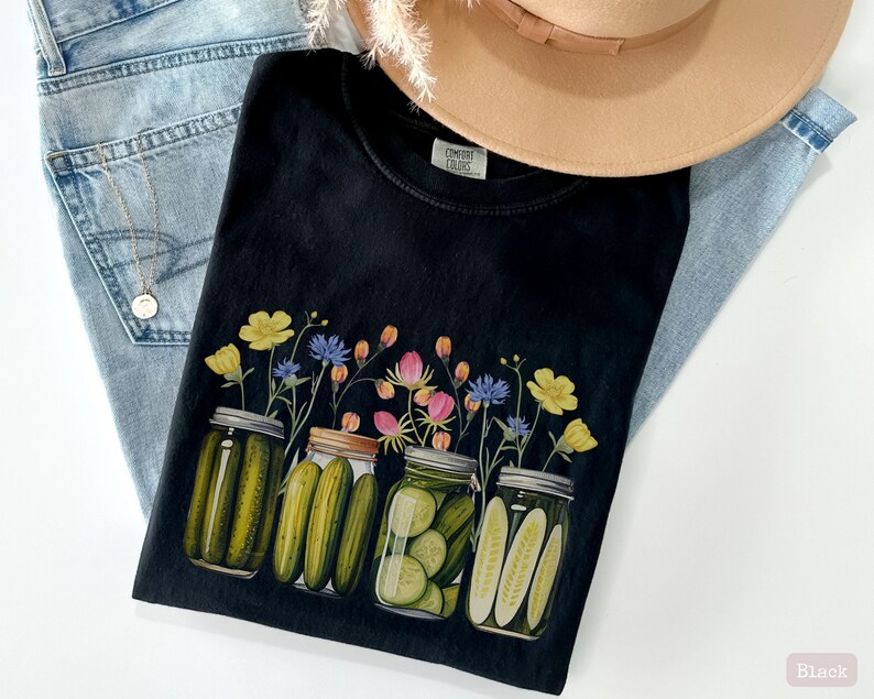 Puede incluir: Camiseta negra con un gr&aacute;fico de cuatro tarros de vidrio llenos de pepinillos y cubiertos de flores silvestres. Las flores son amarillas, rosas, azules y verdes.