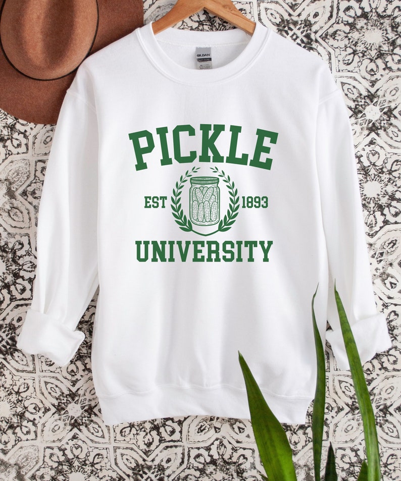 May include: White sweatshirt with green text that reads "Pickle University" with a green pickle jar graphic and the text "Est 1893".