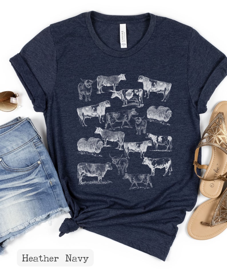 May include: A heather navy blue t-shirt with a white graphic print of various cow breeds. The shirt has a crew neck and short sleeves.