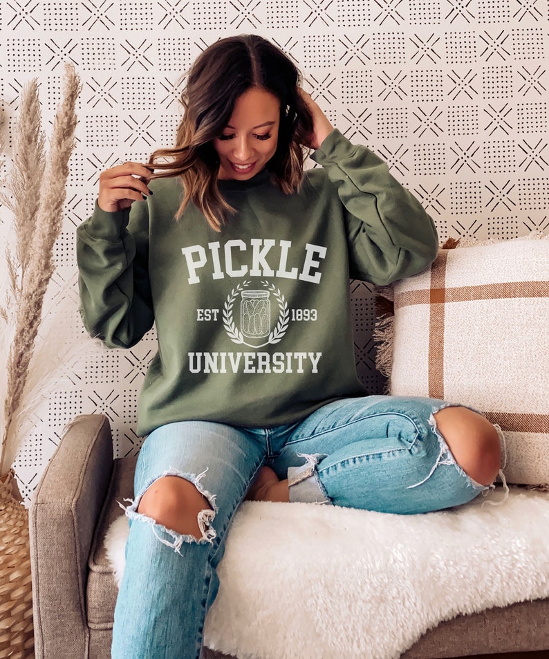 May include: A green sweatshirt with the text "Pickle University" in white, featuring a white illustration of a jar of pickles and the text "Est. 1893".