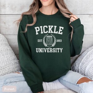 May include: A dark green sweatshirt with white text that reads "Pickle University" with a pickle jar graphic and the text "Est. 1893".