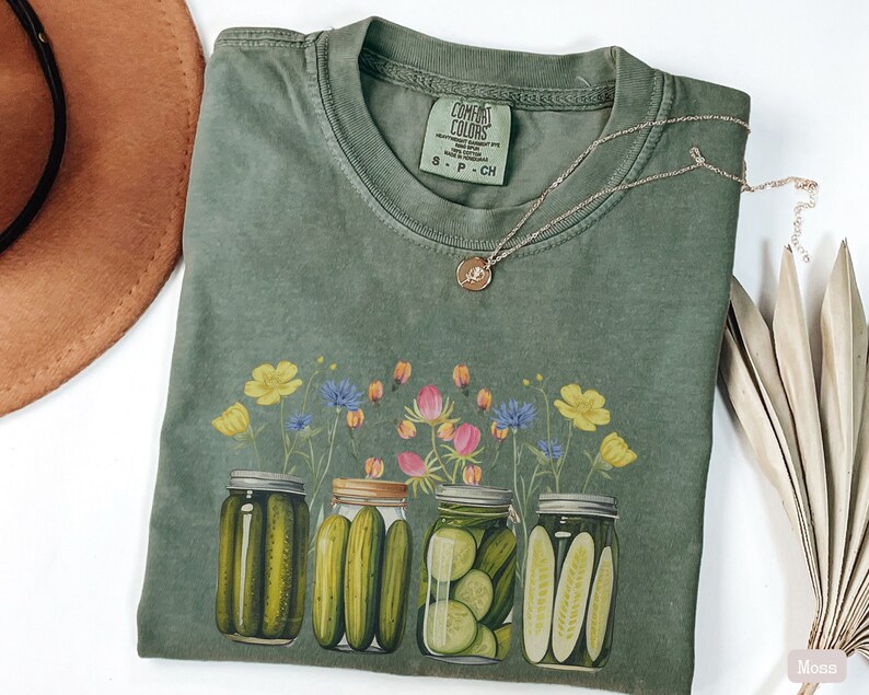Puede incluir: Camiseta verde con un estampado de cuatro botes de pepinillos y flores silvestres. La etiqueta dice "COMFORT COLORS".