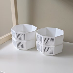 May include: Three white octagonal bowls with black geometric patterns stacked on top of each other. The bowls are on a white surface.