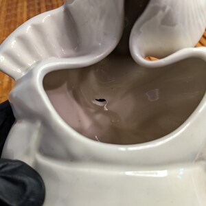 May include: White ceramic planter with a unique, wavy design. The planter has a large opening at the top and a small hole in the bottom for drainage.