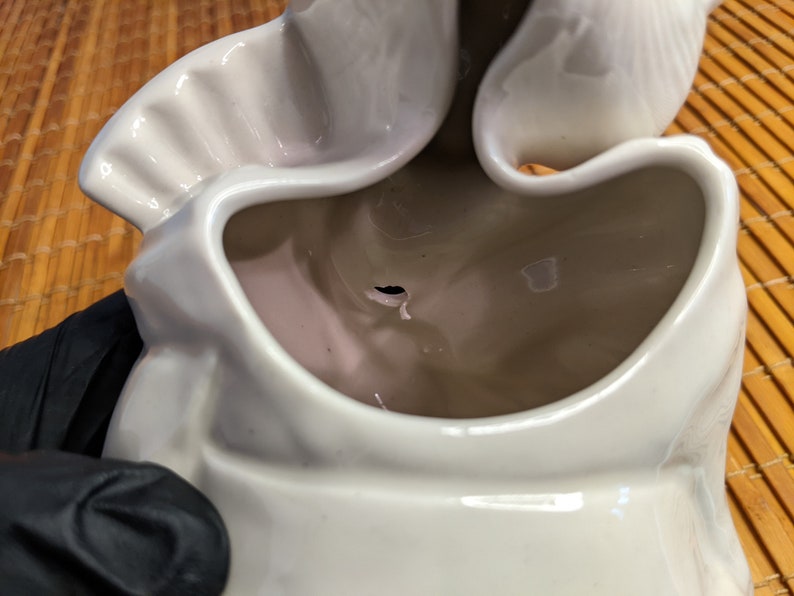 May include: White ceramic planter with a unique, wavy design. The planter has a large opening at the top and a small hole in the bottom for drainage.