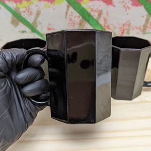 May include: Three black octagonal mugs with handles. The mugs are made of glass and have a shiny finish.