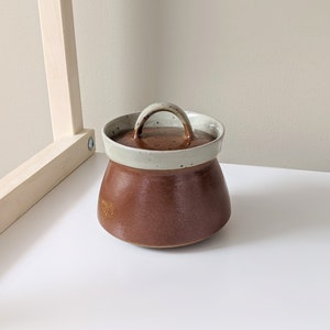 May include: A brown ceramic jar with a white lid and a handle. The jar has a speckled glaze.
