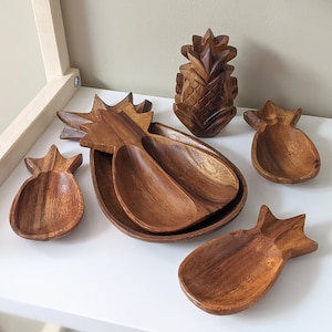 May include: Set of five wooden pineapple-shaped serving dishes. The dishes are made of dark brown wood and have a natural, rustic finish. The dishes are perfect for serving snacks, dips, or appetisers.