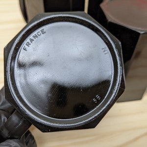 May include: Black octagonal glass mug with a handle. The bottom of the mug has the words "FRANCE" and "3 IN" printed on it.
