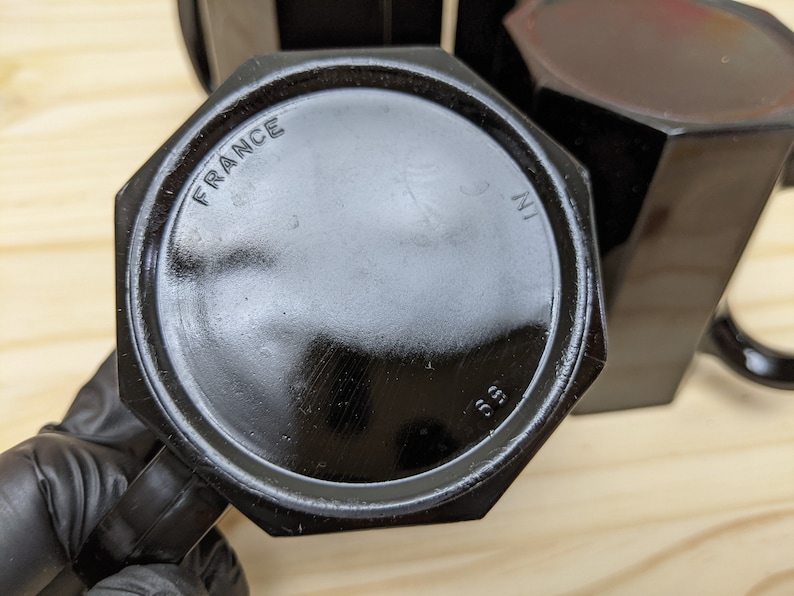 May include: Black octagonal glass mug with a handle. The bottom of the mug has the words "FRANCE" and "3 IN" printed on it.