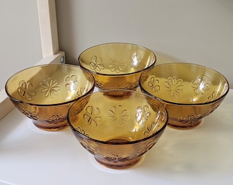 May include: Four amber glass bowls with a floral pattern. The bowls are all the same size and shape, and they are arranged in a row.