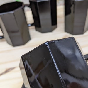 May include: Four black octagonal mugs with handles. The mugs are made of glass and have a shiny finish.