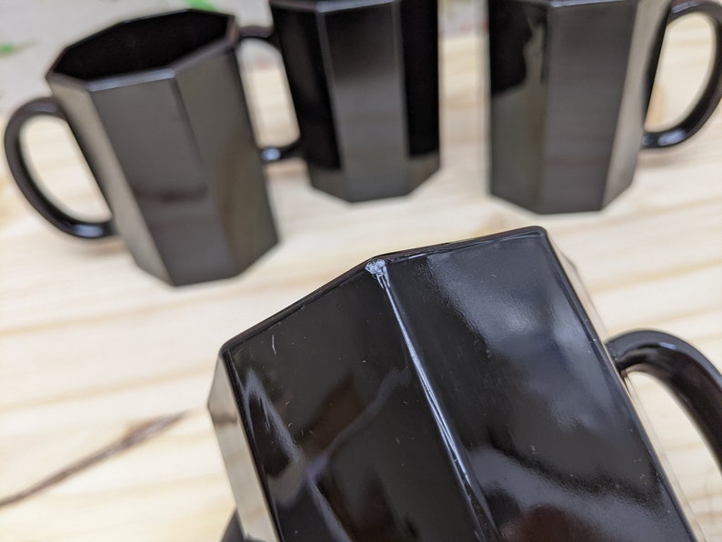 May include: Four black octagonal mugs with handles. The mugs are made of glass and have a shiny finish.