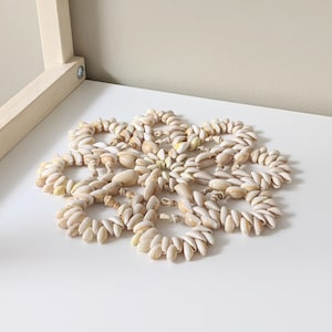 May include: A white seashell coaster with a circular design. The coaster is made of many small seashells that are arranged in a circular pattern.