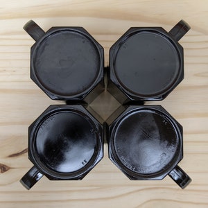 May include: Four black octagonal mugs with handles, viewed from above, on a wooden surface.