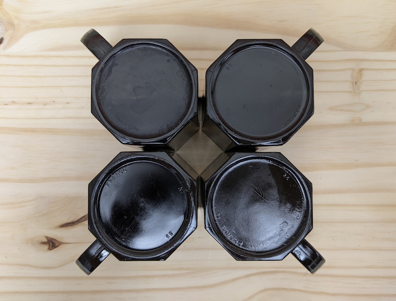 May include: Four black octagonal mugs with handles, viewed from above, on a wooden surface.