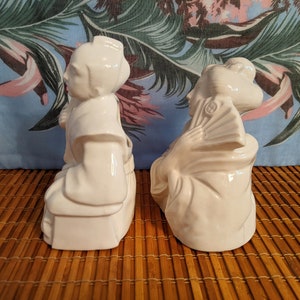 May include: Two white ceramic figurines of people in traditional Japanese clothing. The figurines are sitting on a woven mat.