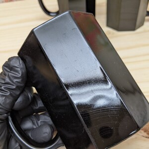 May include: A black hexagonal mug with a glossy finish. The mug has a handle and is made of ceramic.