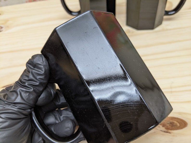 May include: A black hexagonal mug with a glossy finish. The mug has a handle and is made of ceramic.