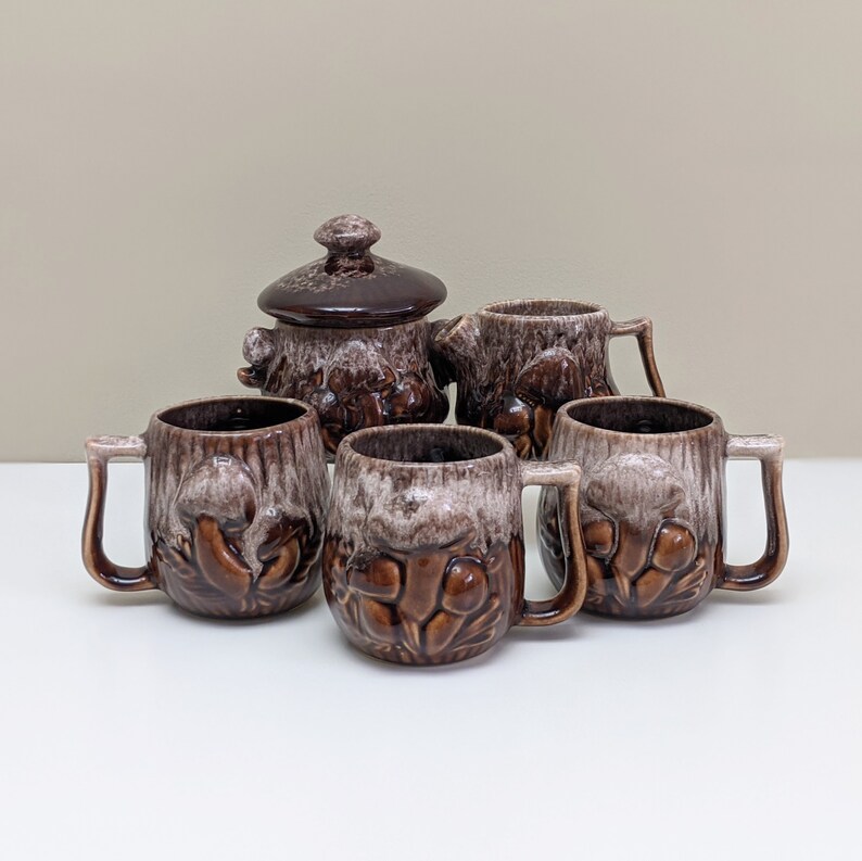 Puede incluir: Conjunto de cinco tazas de cer&aacute;mica marr&oacute;n y blanca con dise&ntilde;os de setas. Las tazas tienen asas y son perfectas para servir bebidas calientes.