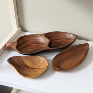 May include: Three wooden serving bowls, one with three sections, one pear-shaped, and one leaf-shaped. The bowls are made of dark brown wood with a natural grain pattern.
